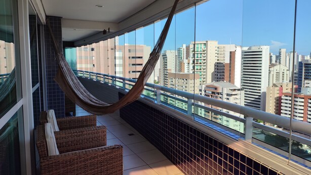 A balcony with a hammock, wicker furniture, and a city view. - Vip Beira Mar Residence (Fortaleza)