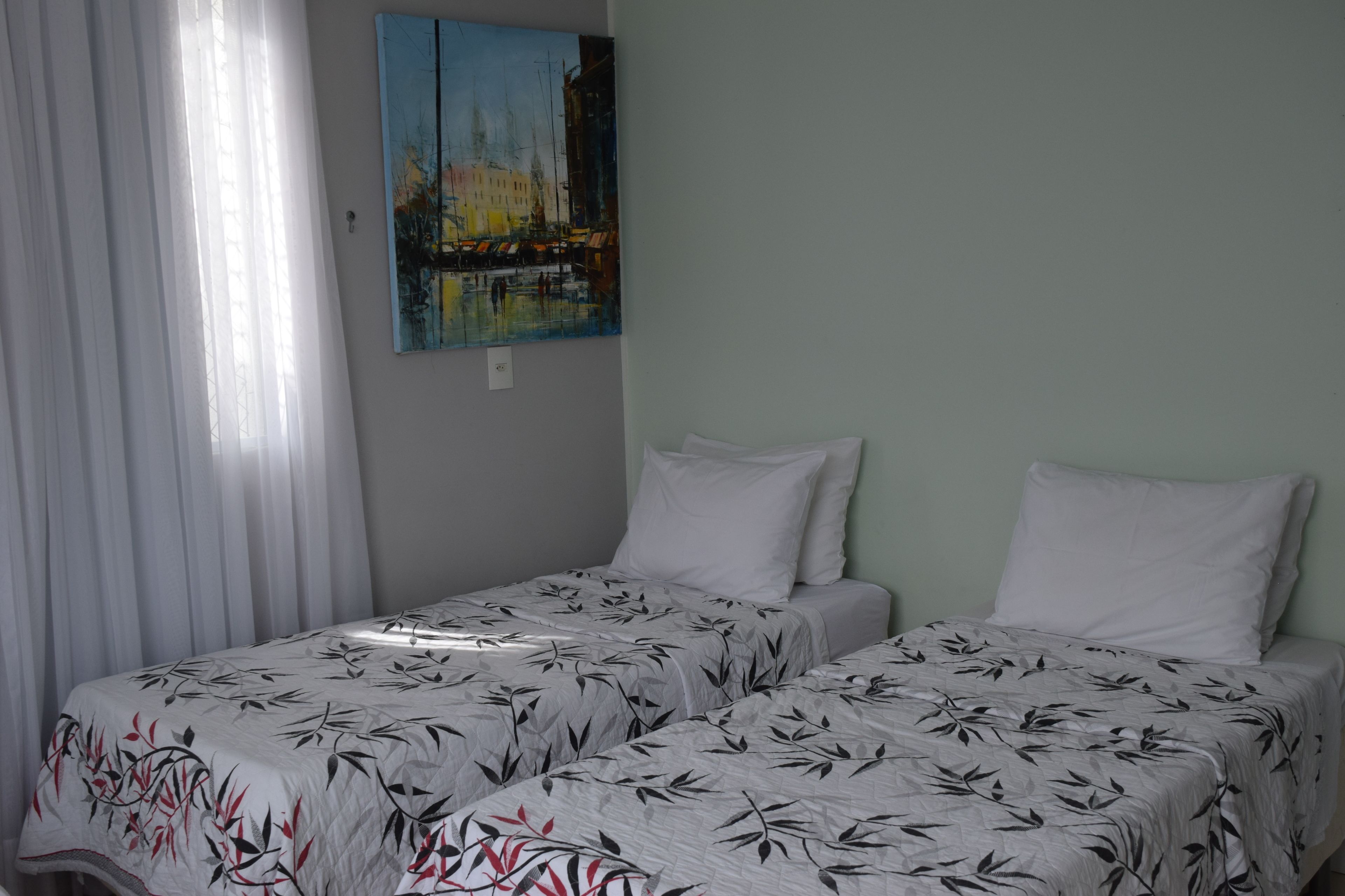 Una stanza con due letti, biancheria da letto bianca, un quadro al muro e una finestra con tende bianche.