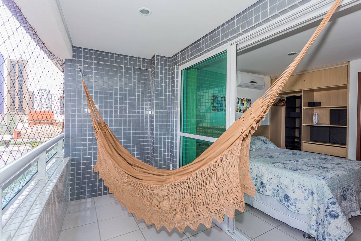 A balcony with a hammock, a bed with a floral bedspread, and a wardrobe.