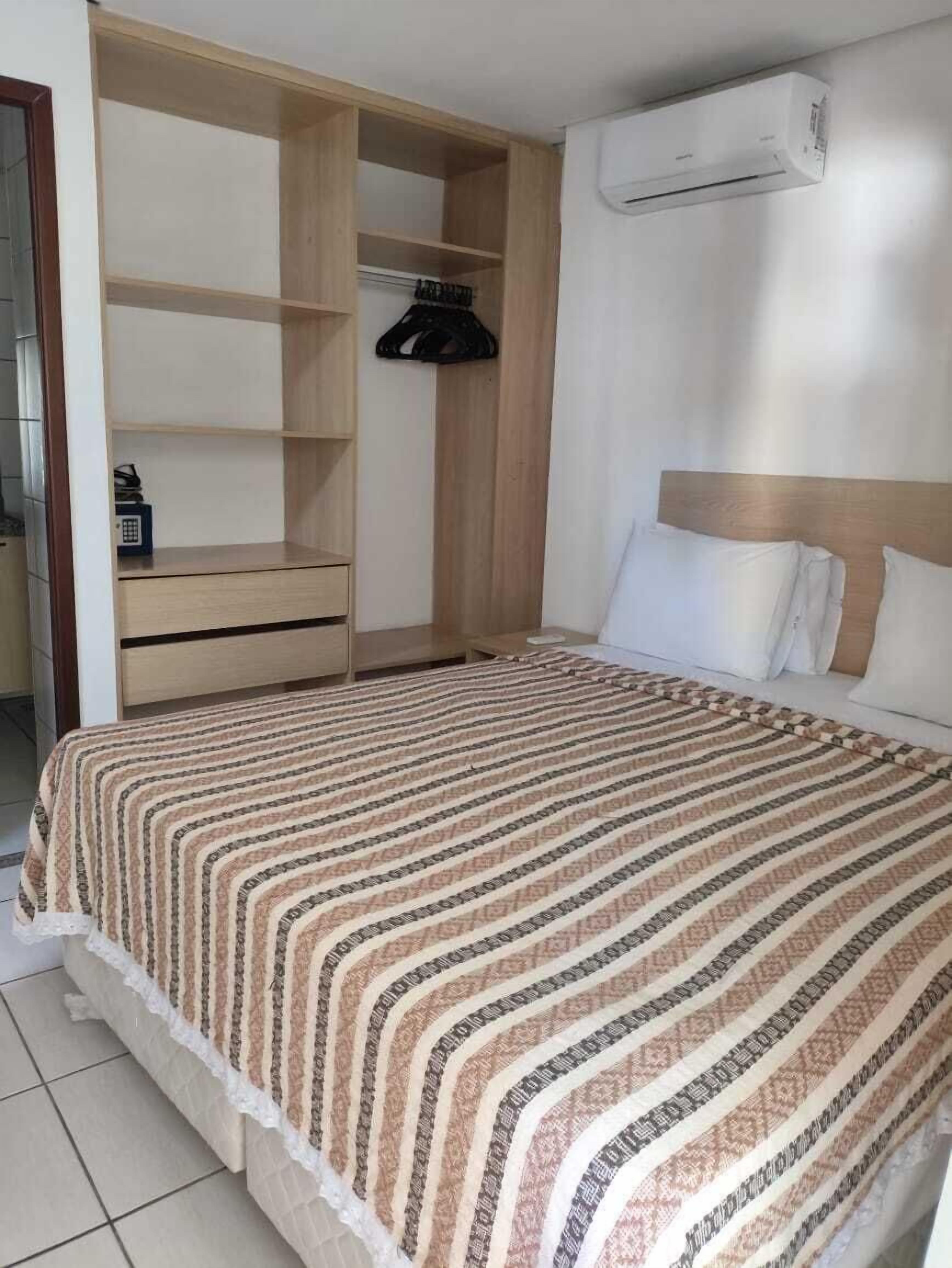 Ein Schlafzimmer mit einem Bett, einem Holzschrank, einer Kleiderstange und einer Klimaanlage.