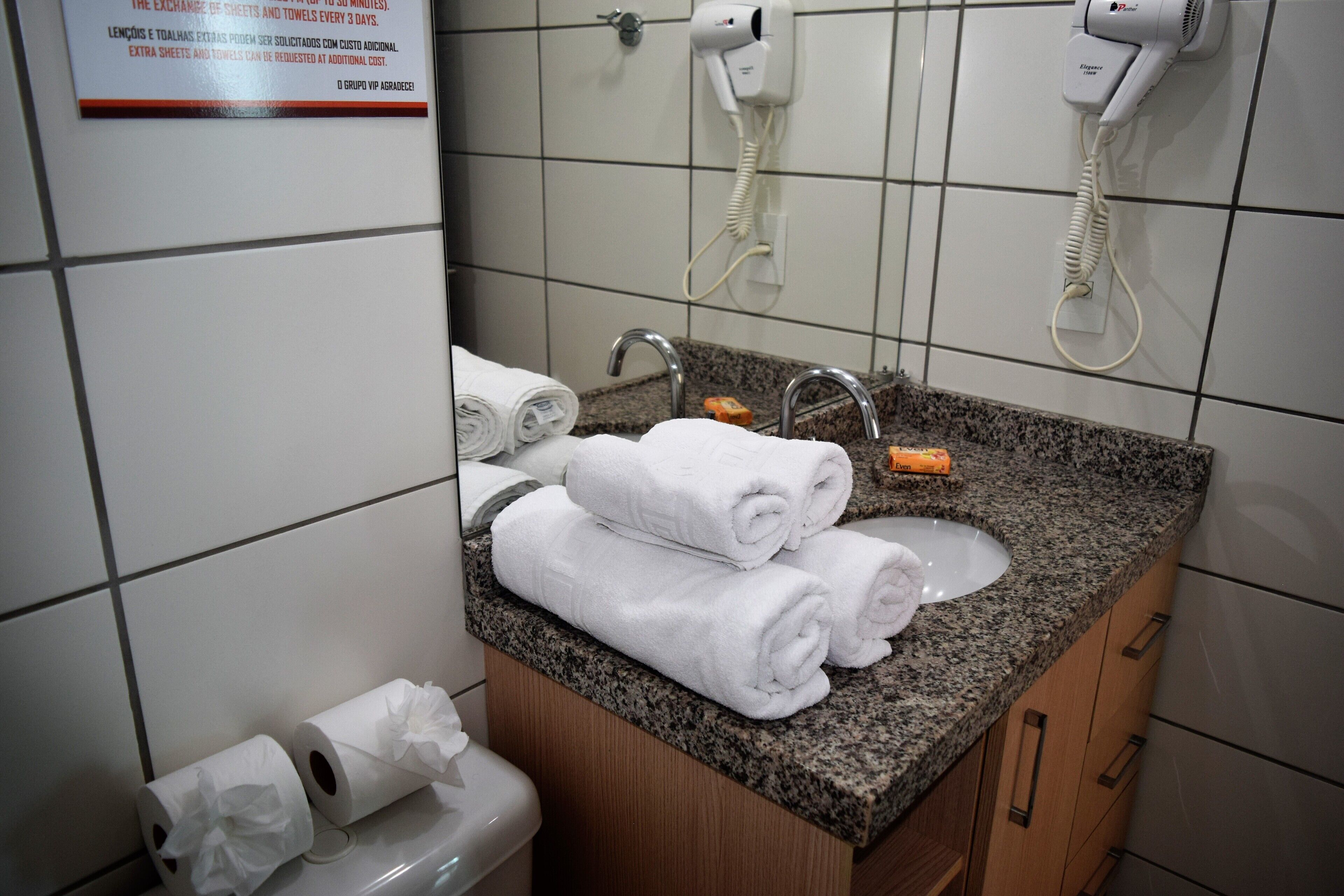 Un baño con encimera de granito, un lavabo y dos secadores de pelo fijados en la pared.