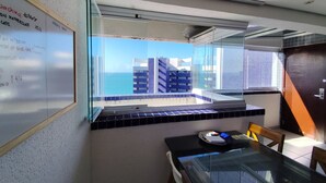 A modern room with a glass table and chairs, a whiteboard with writing, and a view of buildings and the sea. - Vip Beira Mar Residence (Fortaleza)