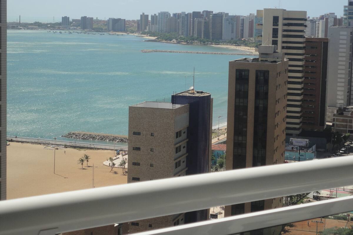 A coastal cityscape with high-rise buildings, a beach, and a clear sky.