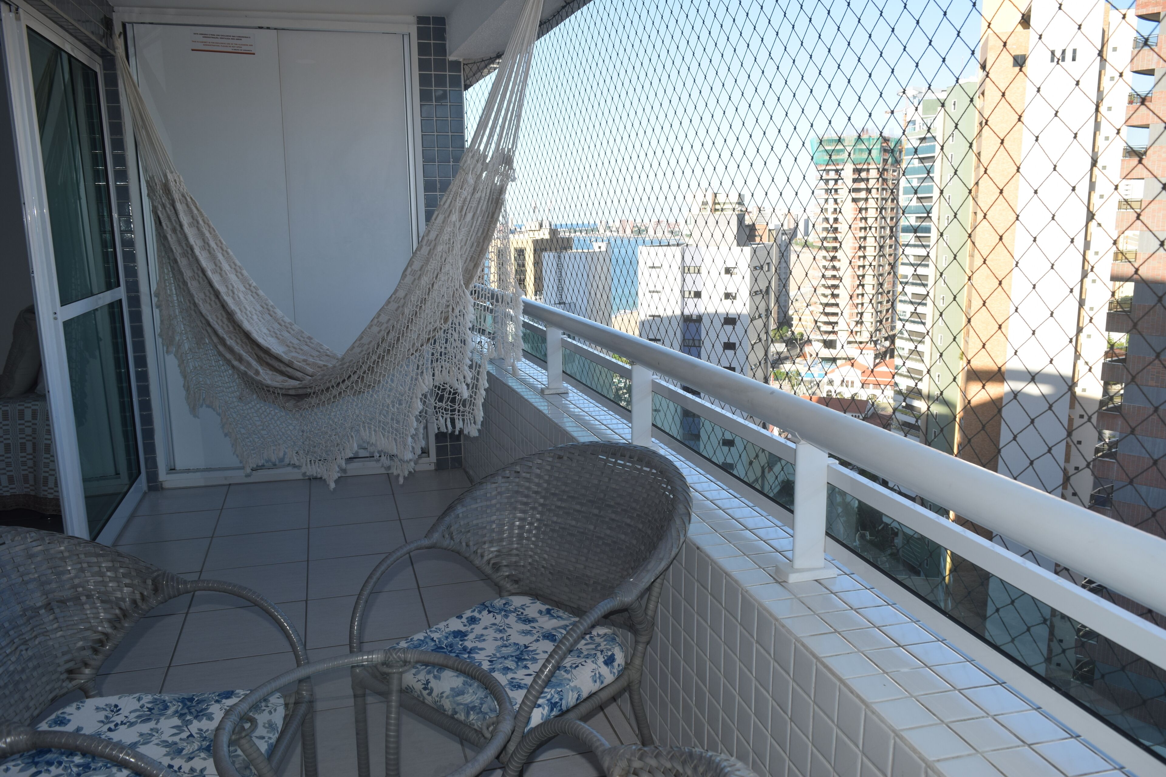 A balcony with wicker chairs and a hammock, overlooking a cityscape with tall buildings.