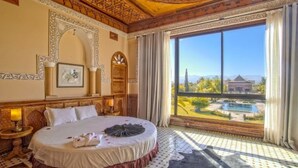 Een luxueuze slaapkamer met een groot bed, een gedecoreerd plafond en uitzicht op een zwembad en het landschap.