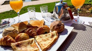 Ontbijt met croissants, toast en sinaasappelsap bij een zwembad, met uitzicht op een gebouw op de achtergrond.