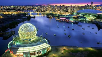 A waterfront view of a cityscape with a large illuminated sphere, a stadium, and boats on the water.