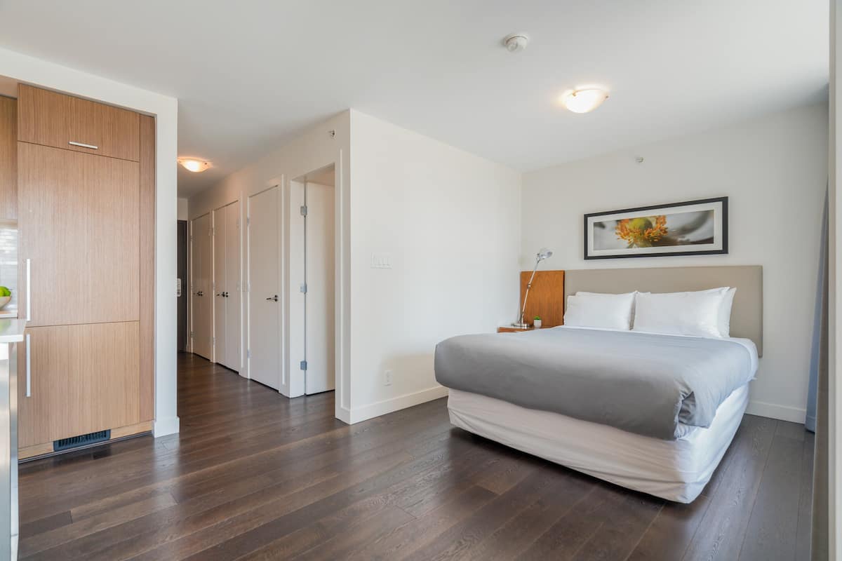 A bedroom with a bed, a nightstand, a framed picture, and a wooden wardrobe.