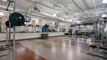 A gym with various exercise equipment, a weight rack, and multiple TV screens displaying workout videos.