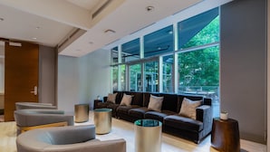 Ein moderner Lounge-Bereich mit einer Sofagarnitur, zwei zylindrischen Beistelltischen und einer Sitzgruppe mit Holzrahmen.