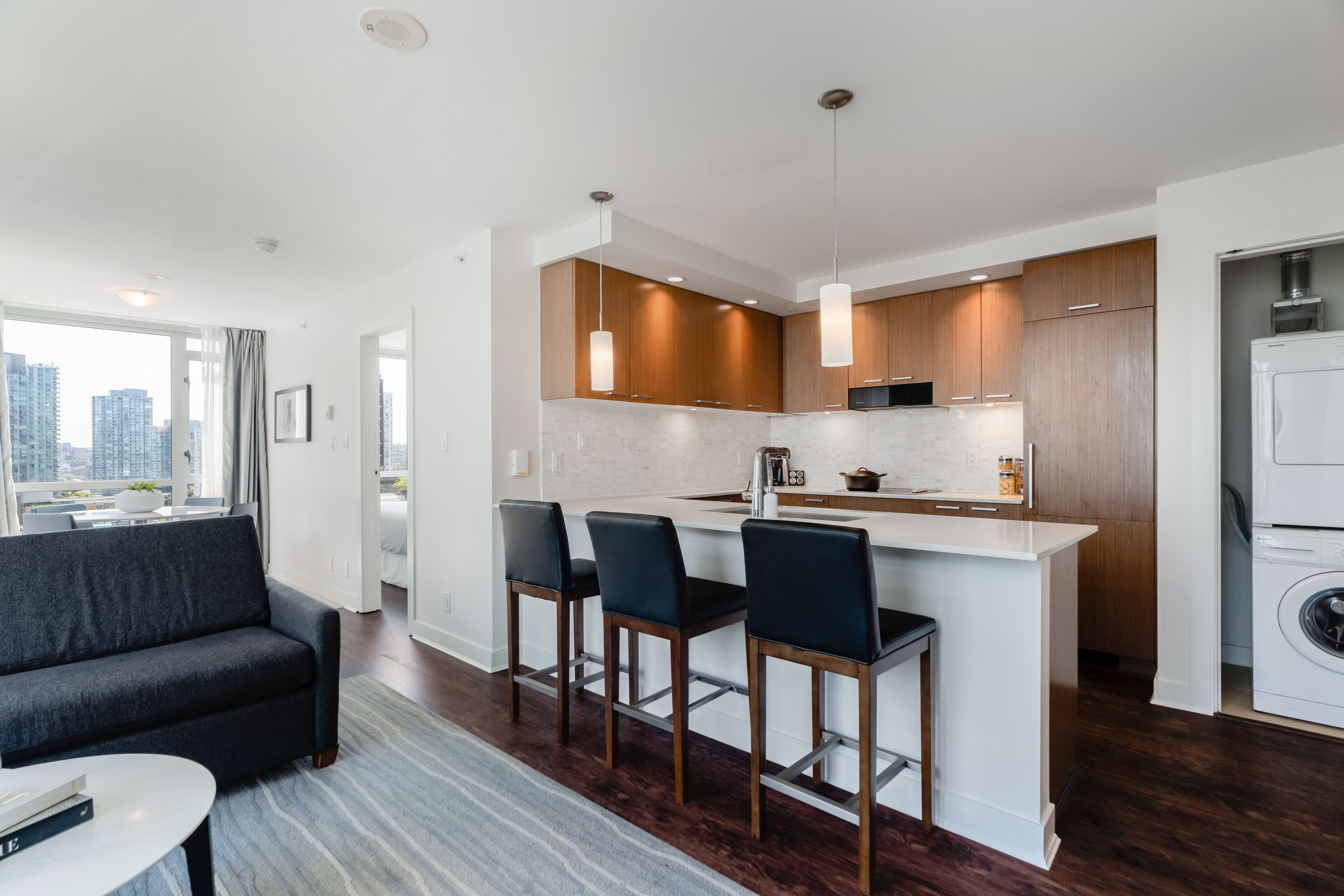 Un apartamento moderno con cocina, comedor y sala de estar. Cuenta con un gran ventanal, un sofá y una barra con taburetes.