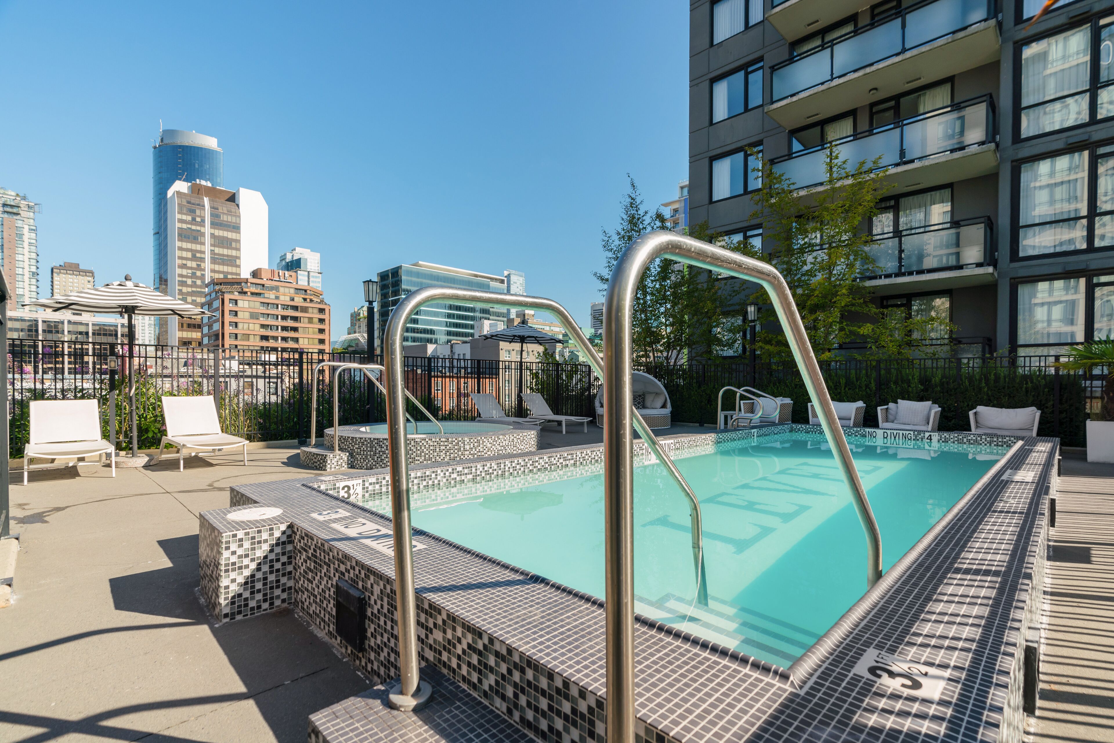 Piscina en la azotea con vista panorámica de la ciudad, sillas de descanso y terraza con baldosas.