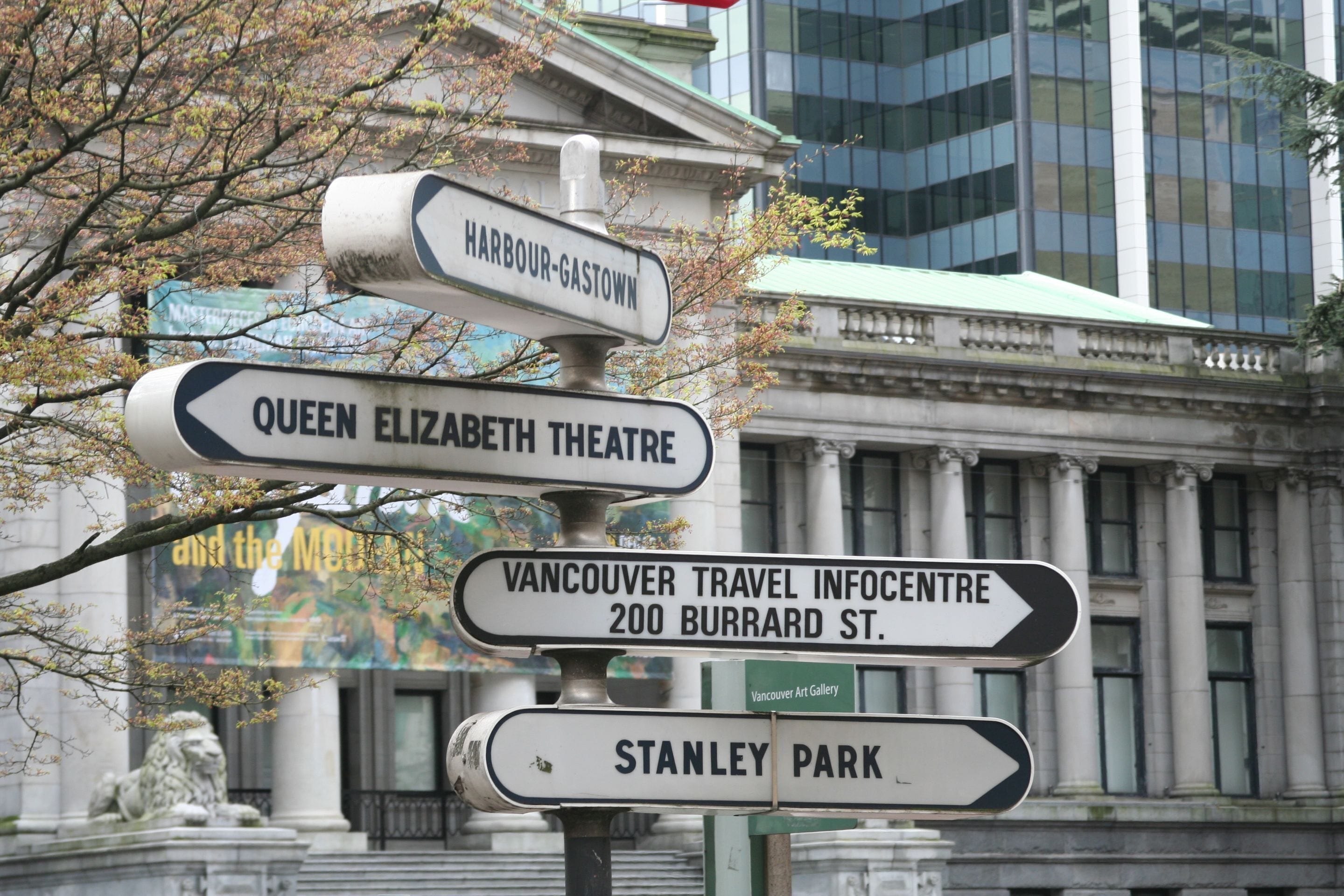 A street sign with multiple directions to landmarks such as Queen Elizabeth Theatre, Vancouver Travel Infocentre, and Stanley Park.