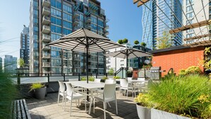 Eine Dachterrasse mit Sitzgelegenheiten im Freien, einem Grill und Blick auf hohe Gebäude.