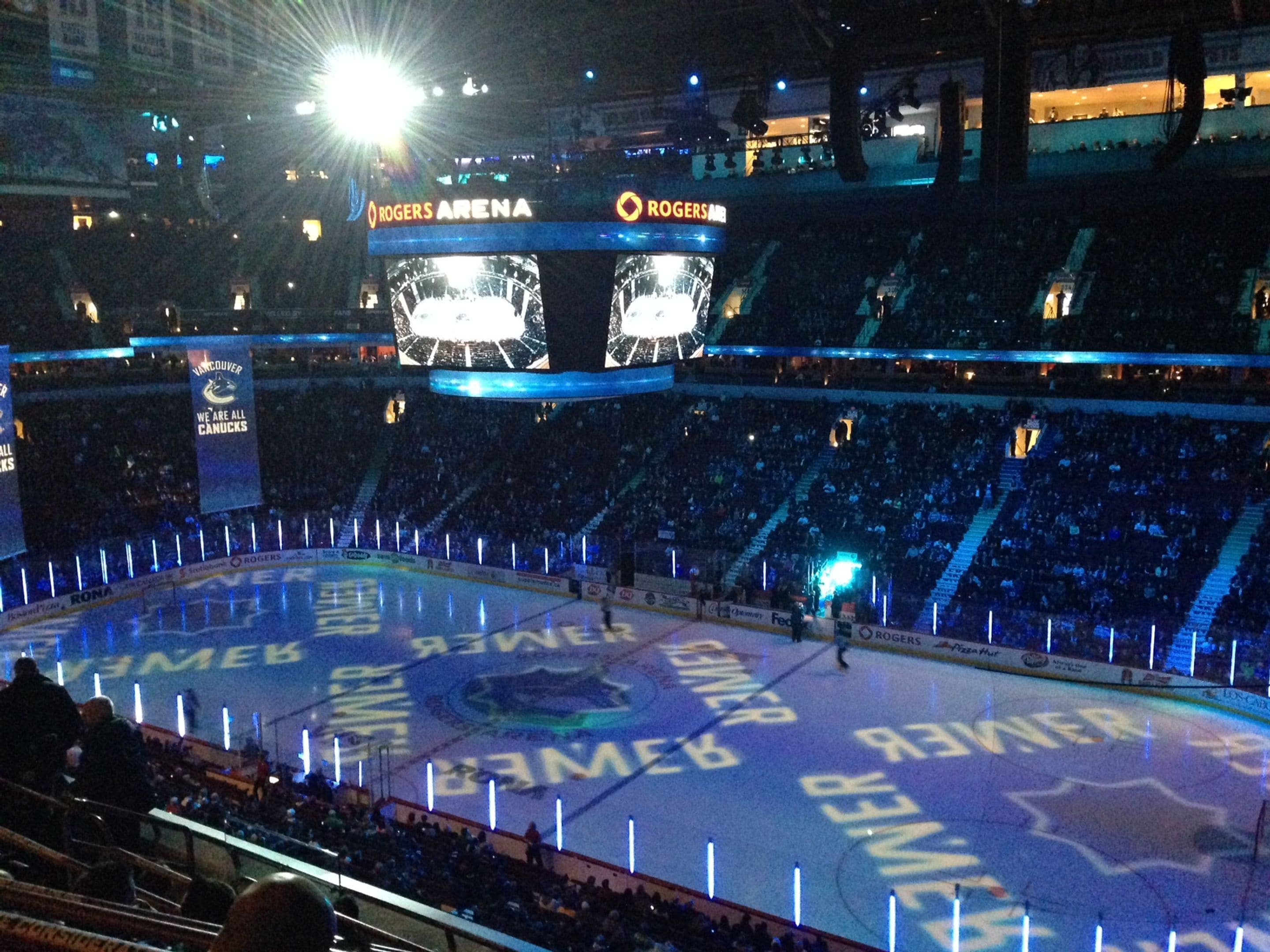 An indoor arena with multiple levels of seating, a large central ice rink, and a scoreboard.