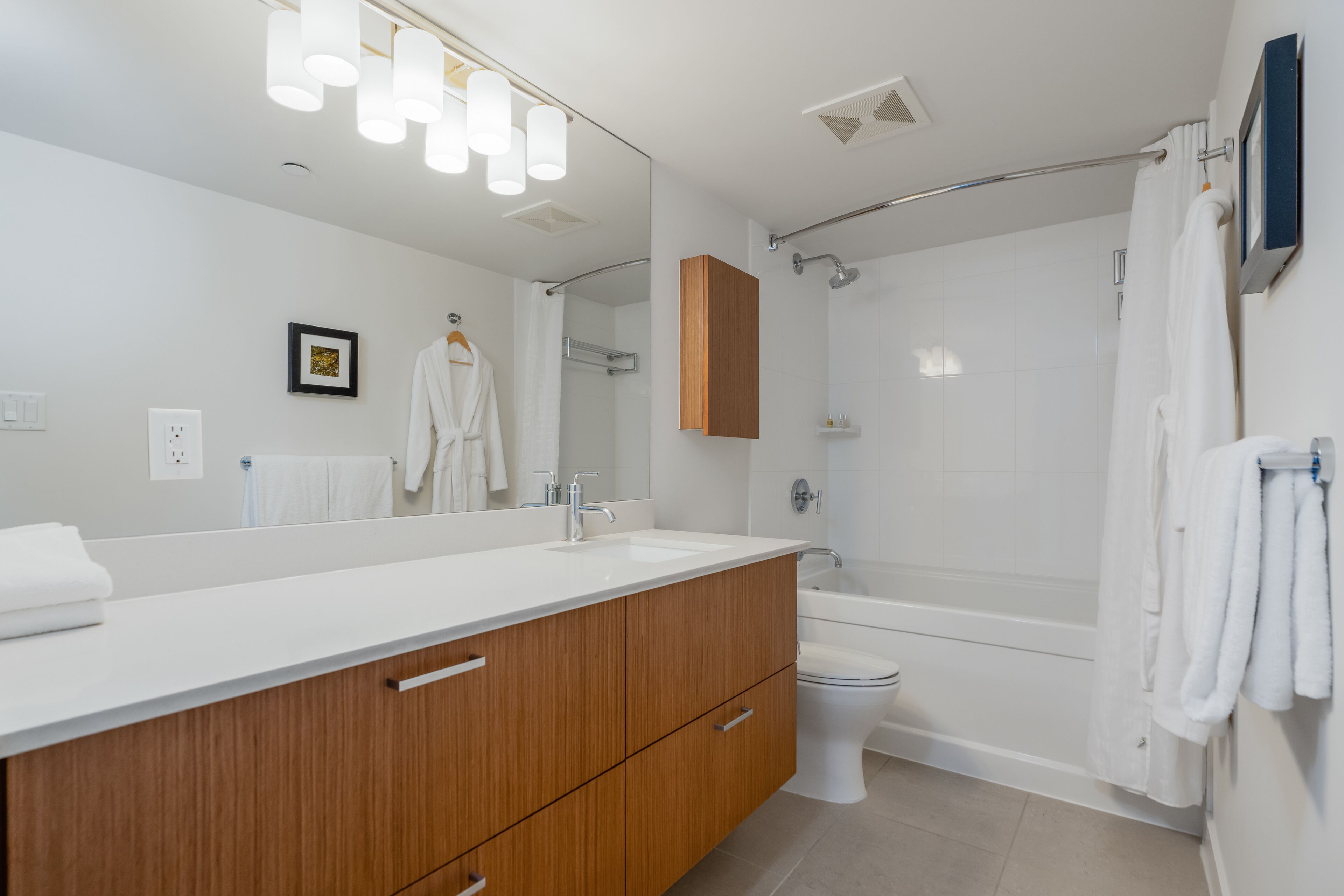 A modern bathroom with a wooden vanity, a large mirror, a bathtub, and a toilet.