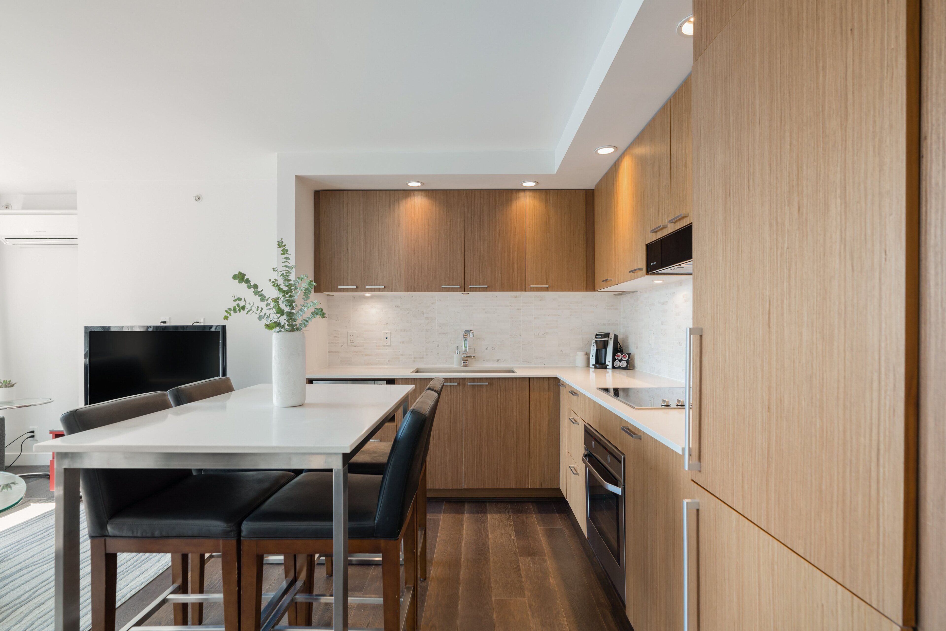 Une cuisine moderne avec des meubles en bois, un plan de travail blanc et un coin repas comprenant une table et des chaises.
