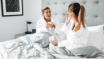Un dormitorio con cama, almohadas, una mesita de noche con lámpara y un cuadro en la pared.