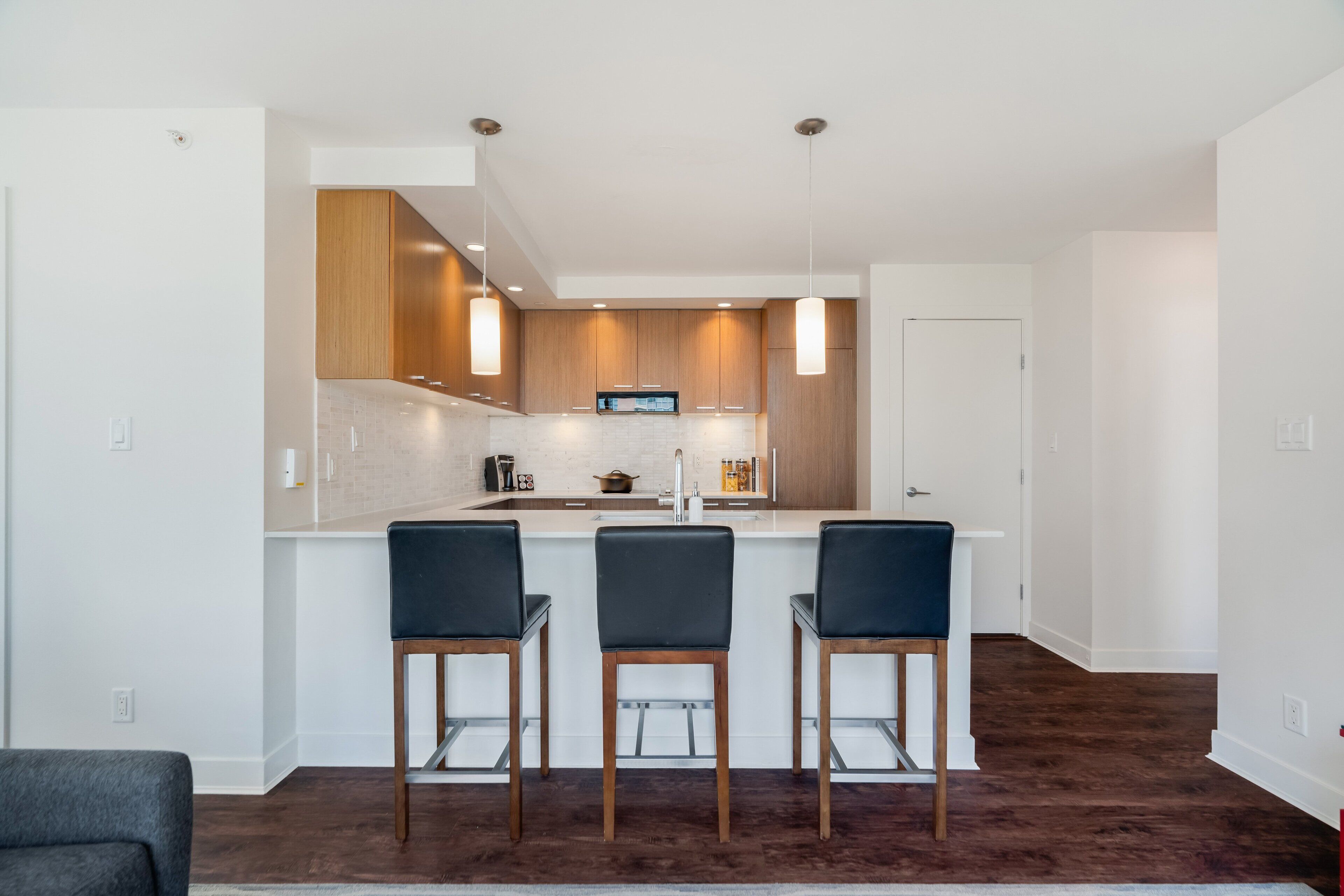 A modern kitchen with a central island, wooden cabinets, and pendant lighting.