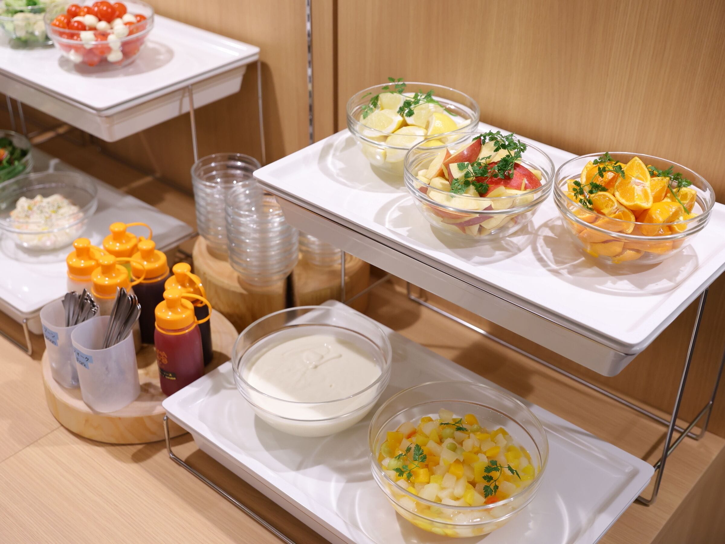 A buffet setup with various food items including fruit salads, a white sauce, and condiments.