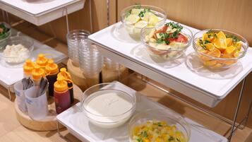 A buffet setup with various food items including fruit salads, a white sauce, and condiments.