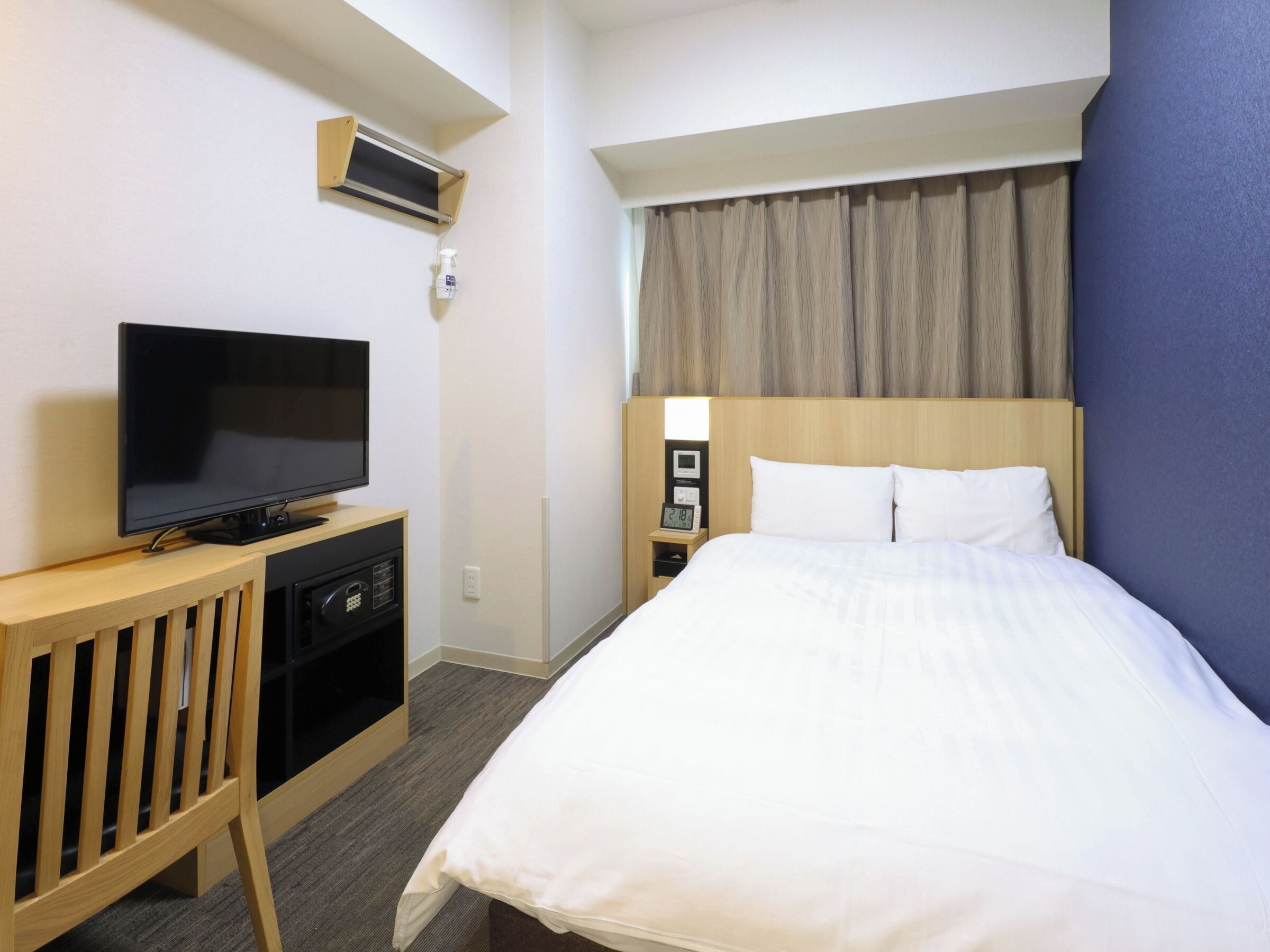 Ein Hotelzimmer mit einem Bett, einem Fernseher auf einem Holztischchen, einem Nachttisch mit einer Uhr und einer Wand-Klimaanlage.