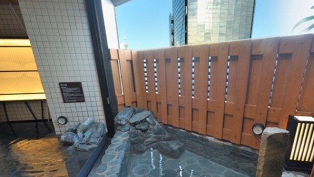 A stone-lined hot tub area with a wooden fence, a stone wall, and a tiled floor. - Dormy Inn Ueno Okachimachi Hot Spring (Tokyo)