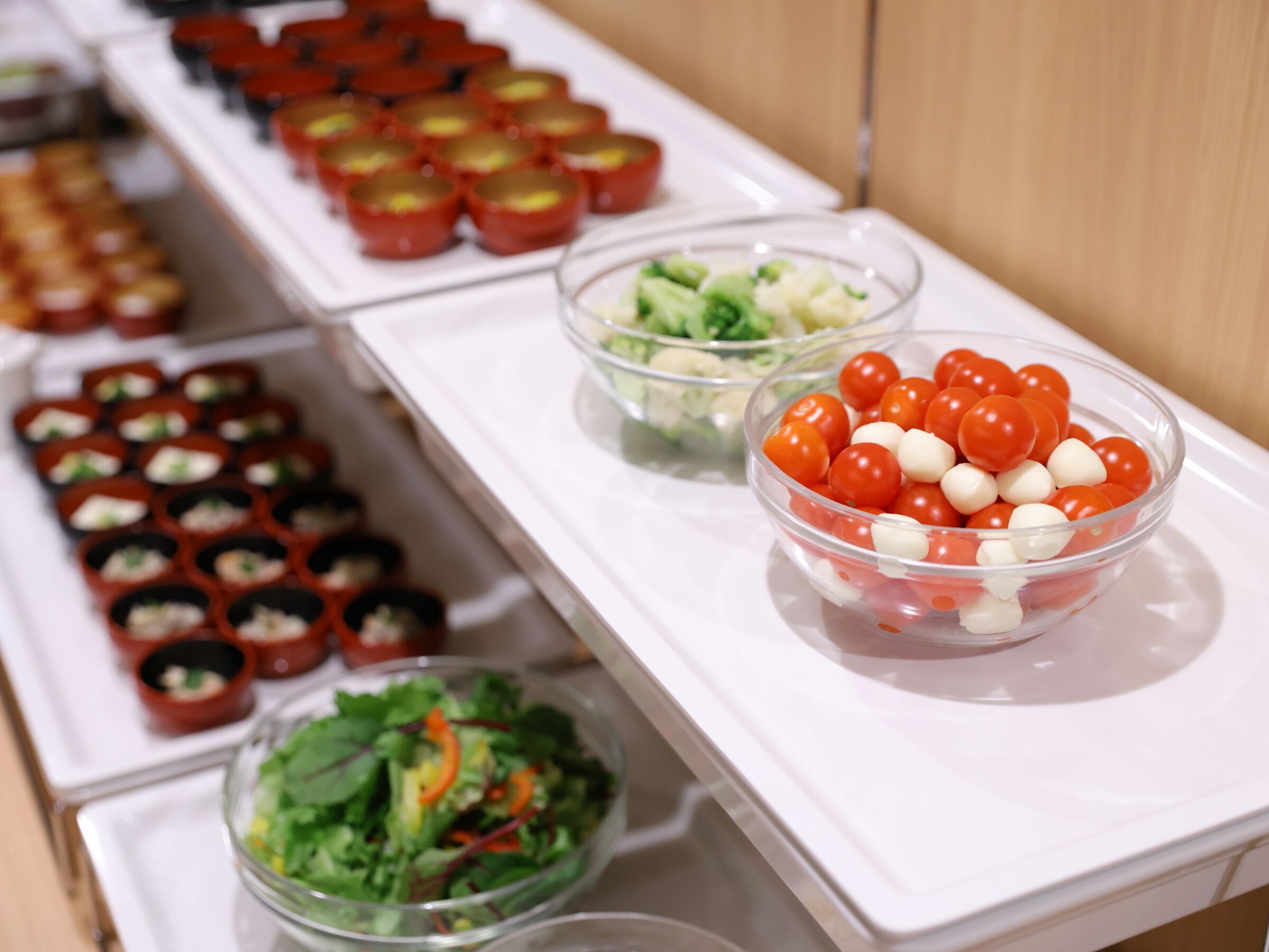 A buffet table with various food items including a bowl of cherry tomatoes and mozzarella balls, a bowl of salad, and several small cups of food.