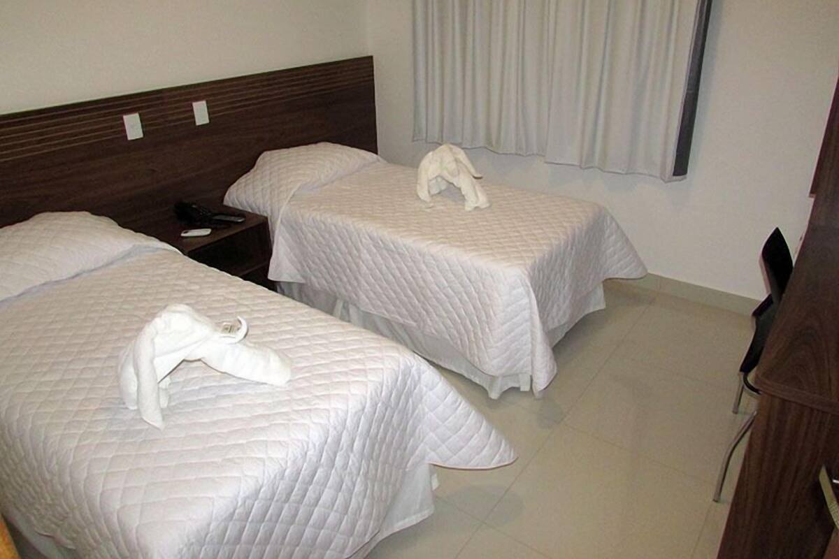 A hotel room with two beds, a wooden headboard, a nightstand, and a window with curtains.