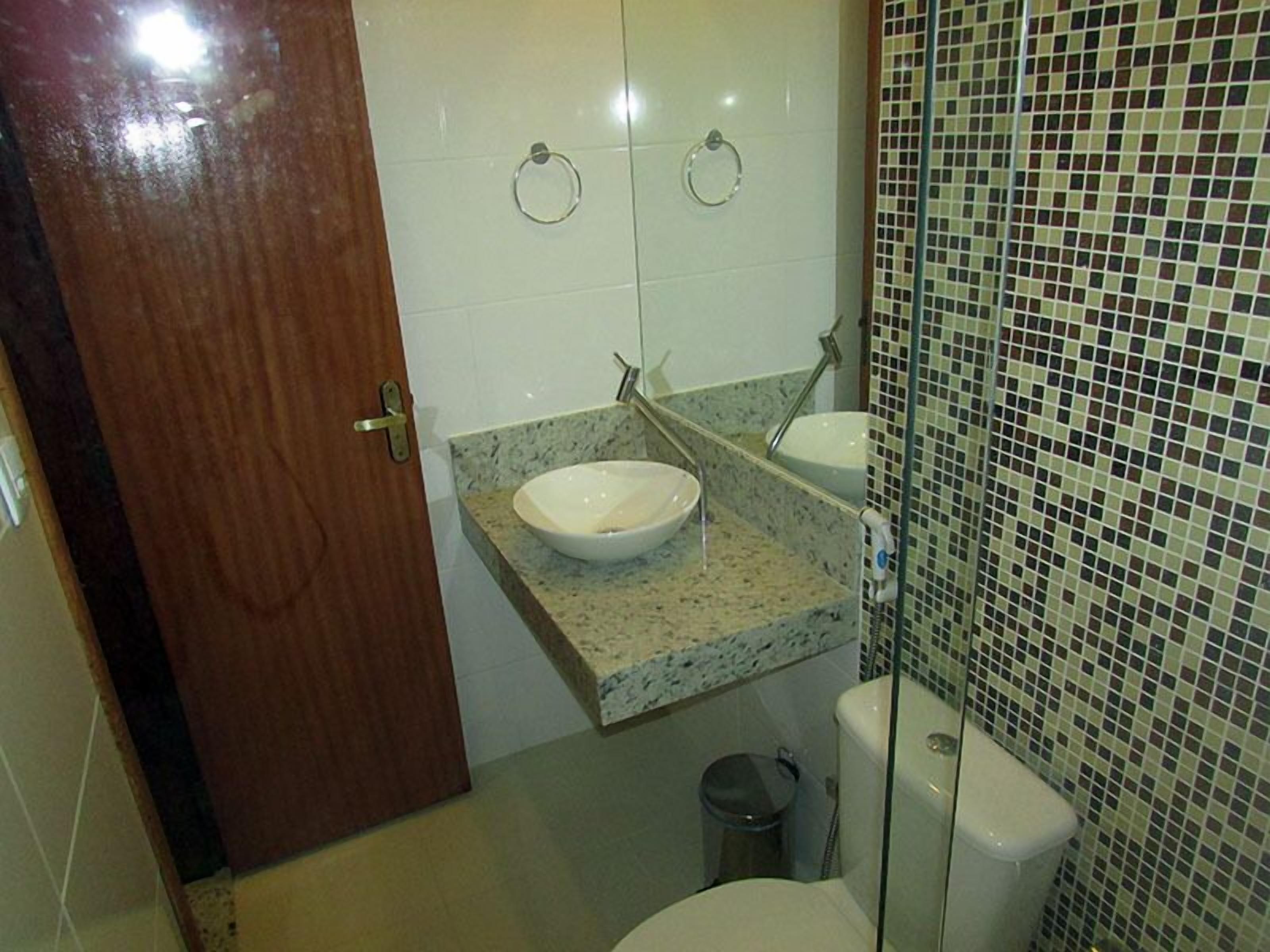A bathroom with a marble countertop, a white sink, a toilet, and a trash bin.