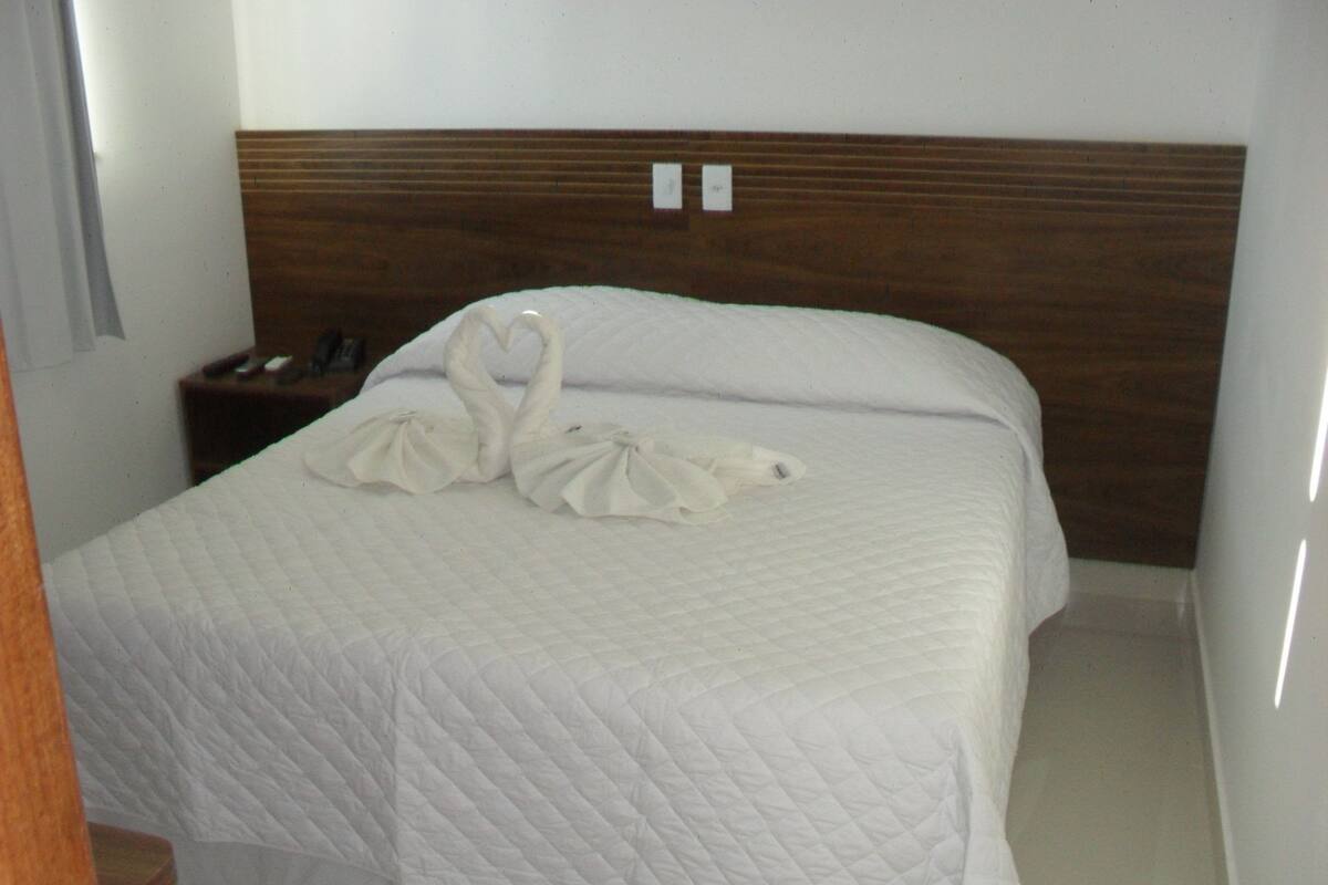 A neatly made bed with a quilted white duvet, a wooden headboard, and two swan-shaped towels on the bed.