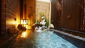 Une source thermale intérieure de style japonais traditionnel, avec un sol en pierre, des murs en bois et un plafond carrelé.