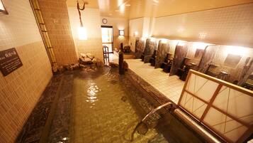 Ein öffentlicher Badebereich mit einem steingefliesten Pool, mehreren Waschbecken und einer hölzernen Bank.