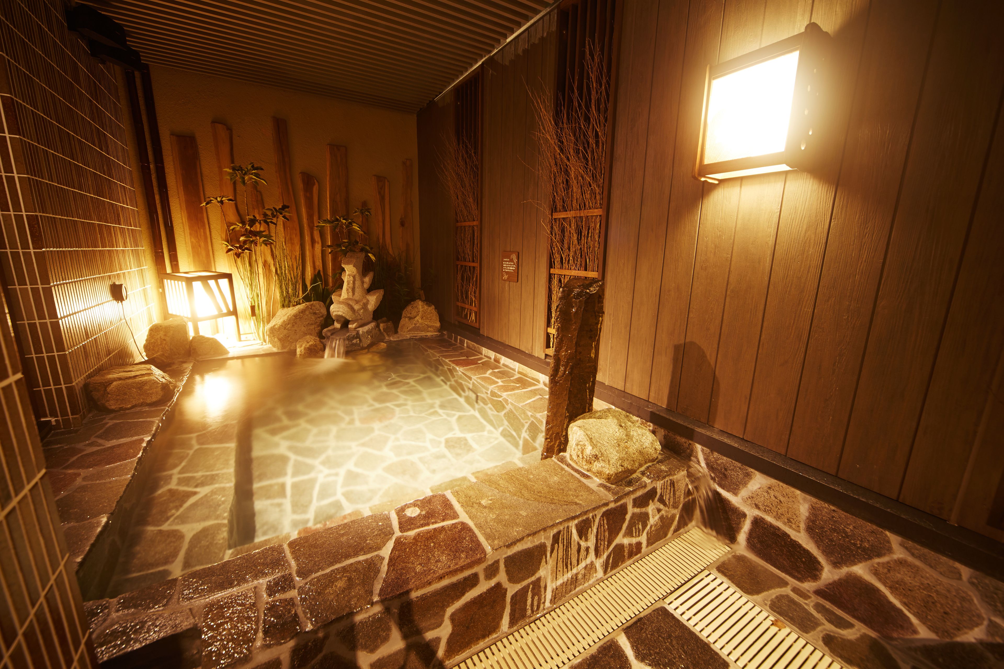 A traditional Japanese onsen with stone flooring, wooden walls, and a stone bath area.