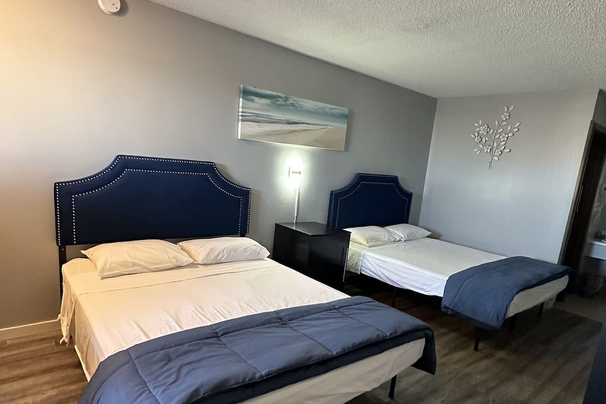 A hotel room with two beds, a nightstand, a wall-mounted lamp, and a decorative wall piece.