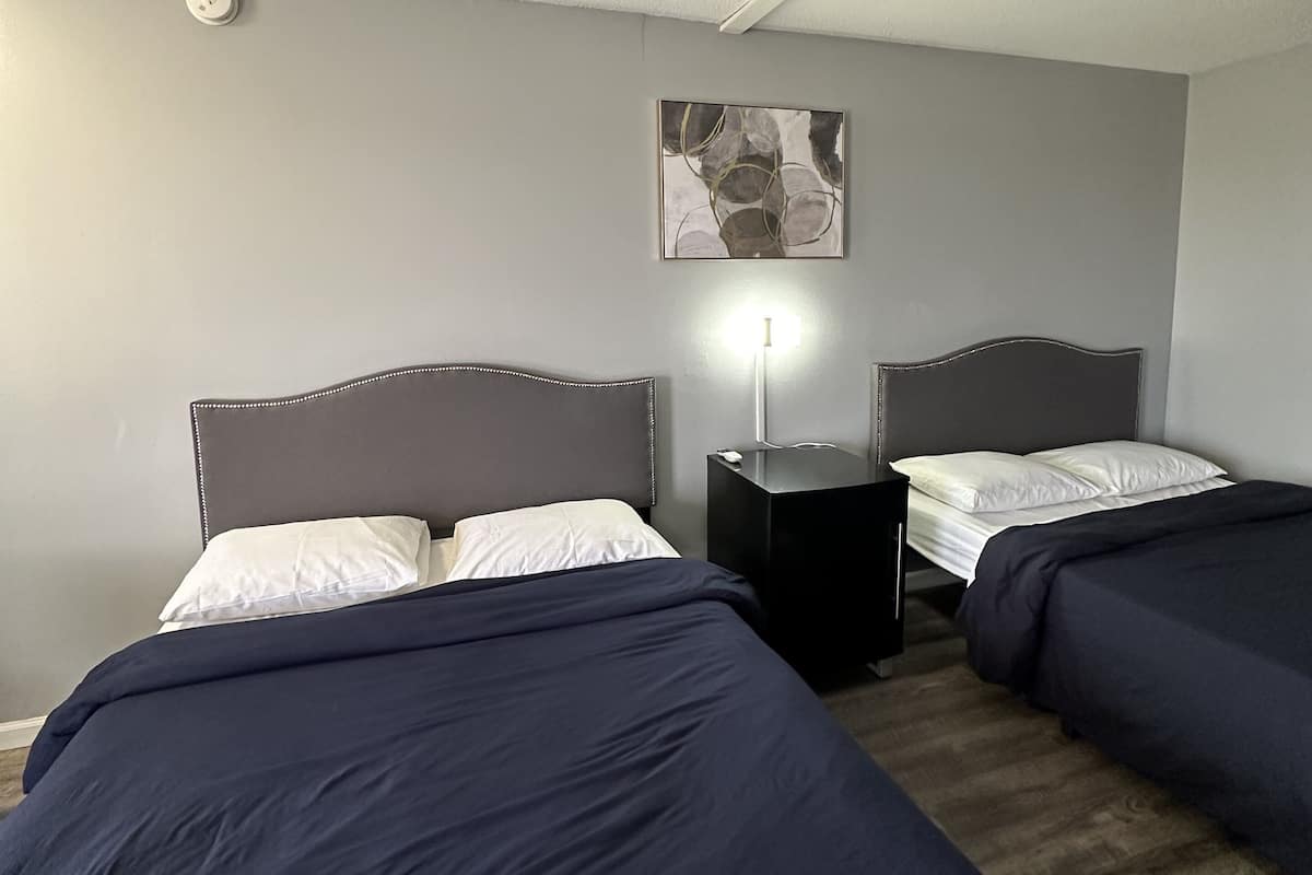 A hotel room with two beds, a nightstand, a wall-mounted light, and a ceiling-mounted smoke detector.