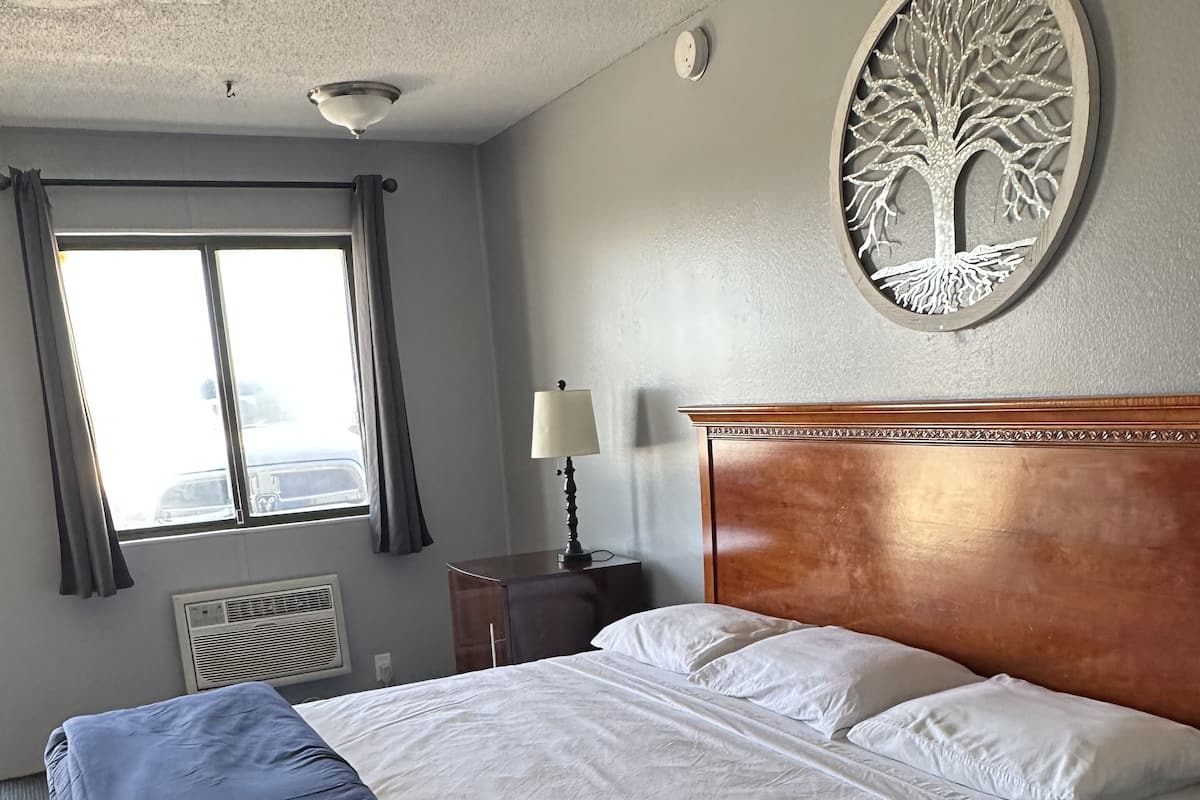 A hotel room with a large bed, a nightstand, a lamp, a window with curtains, and a wall decoration.