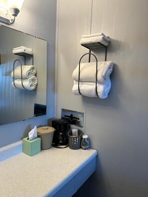A bathroom with a mirror, towel racks, a coffee machine, and toiletries on the counter. - Paxton Inn Motel (Paxton)