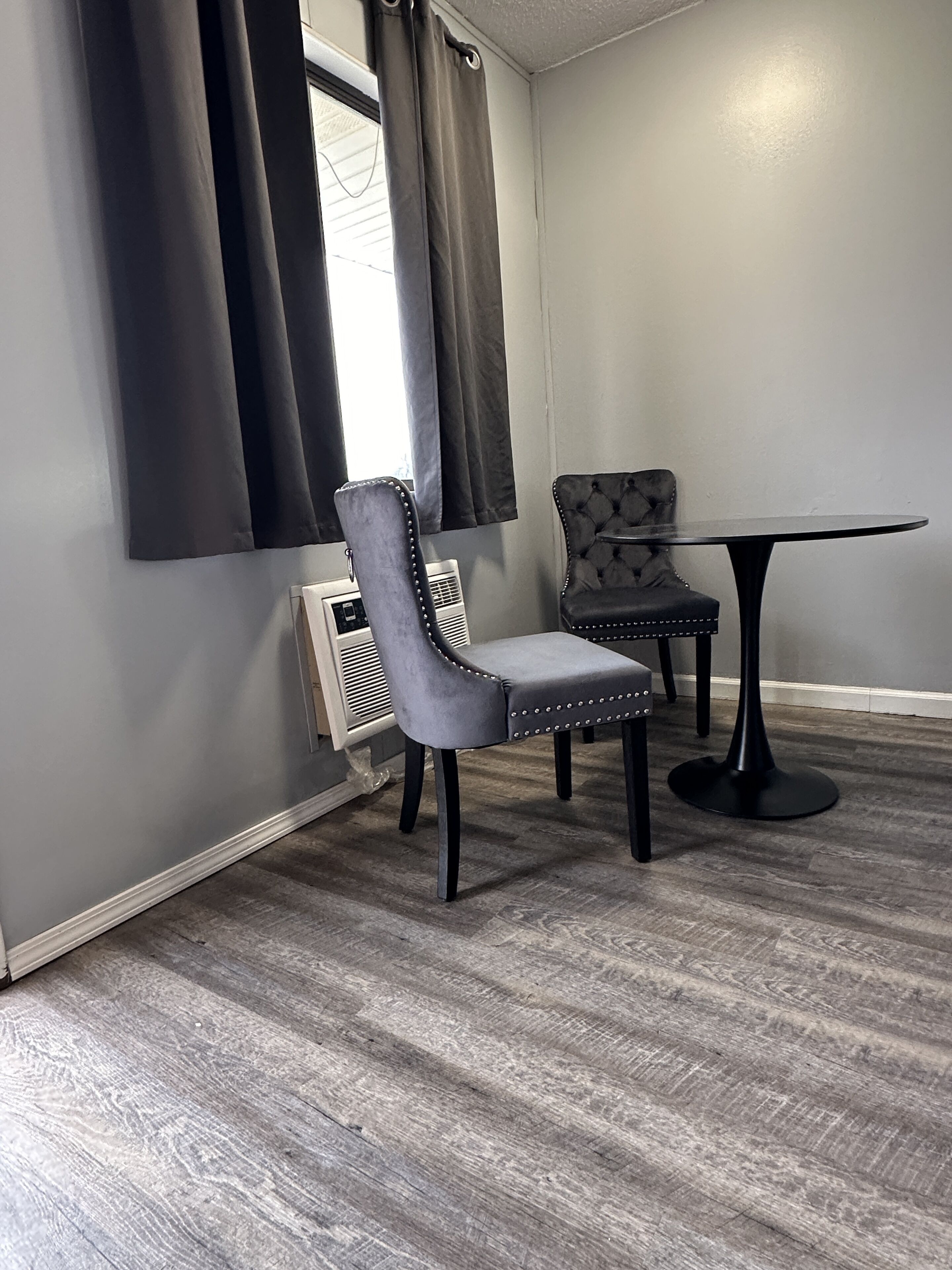 A room with a grey upholstered chair, a matching armchair, and a round table.