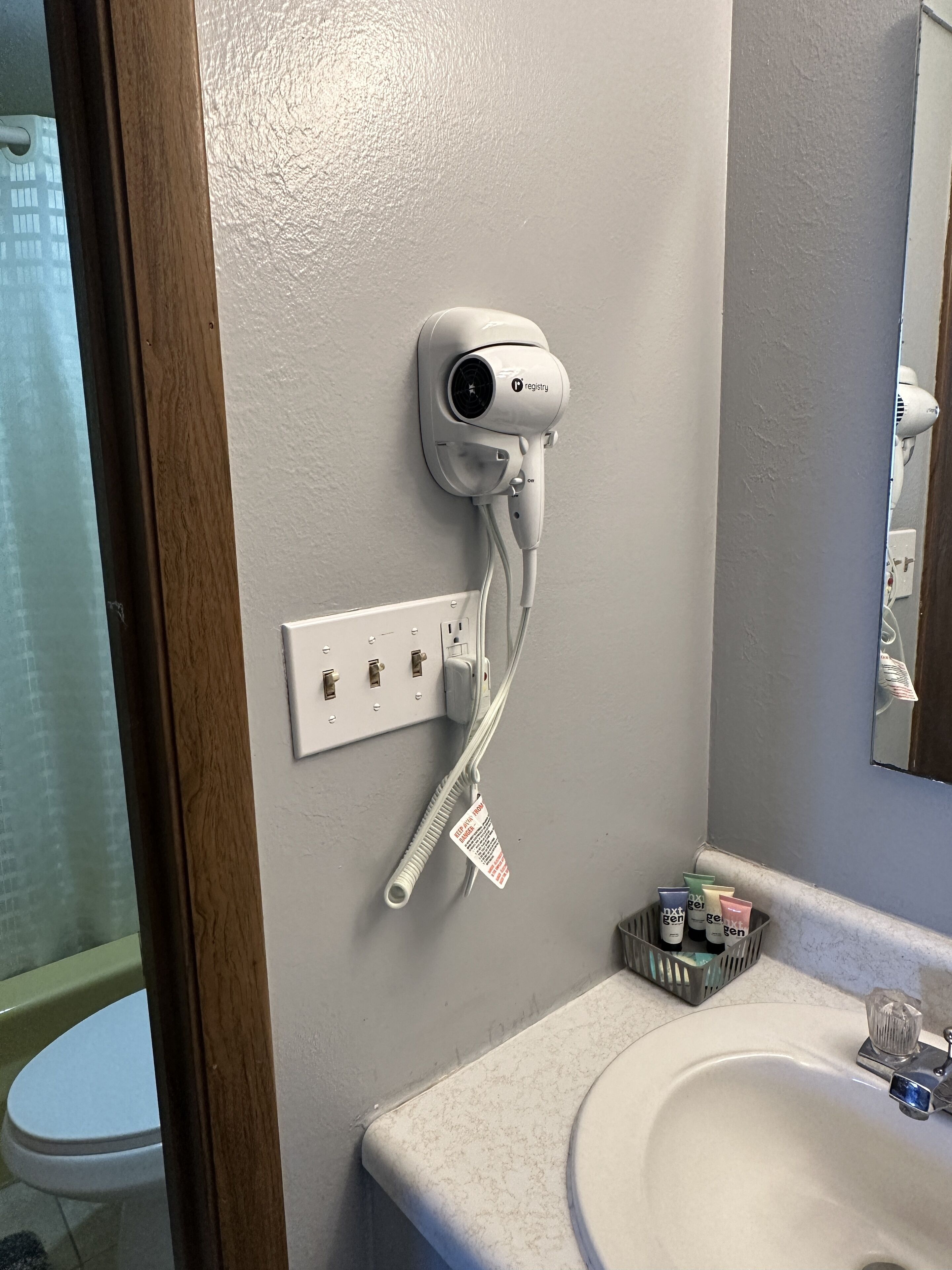 A bathroom with a white sink, a hairdryer mounted on the wall, and a small basket of toiletries.