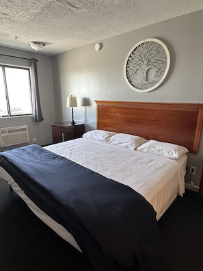 A hotel room with a large bed, a round wall decoration, a window with curtains, and a bedside table with a lamp.