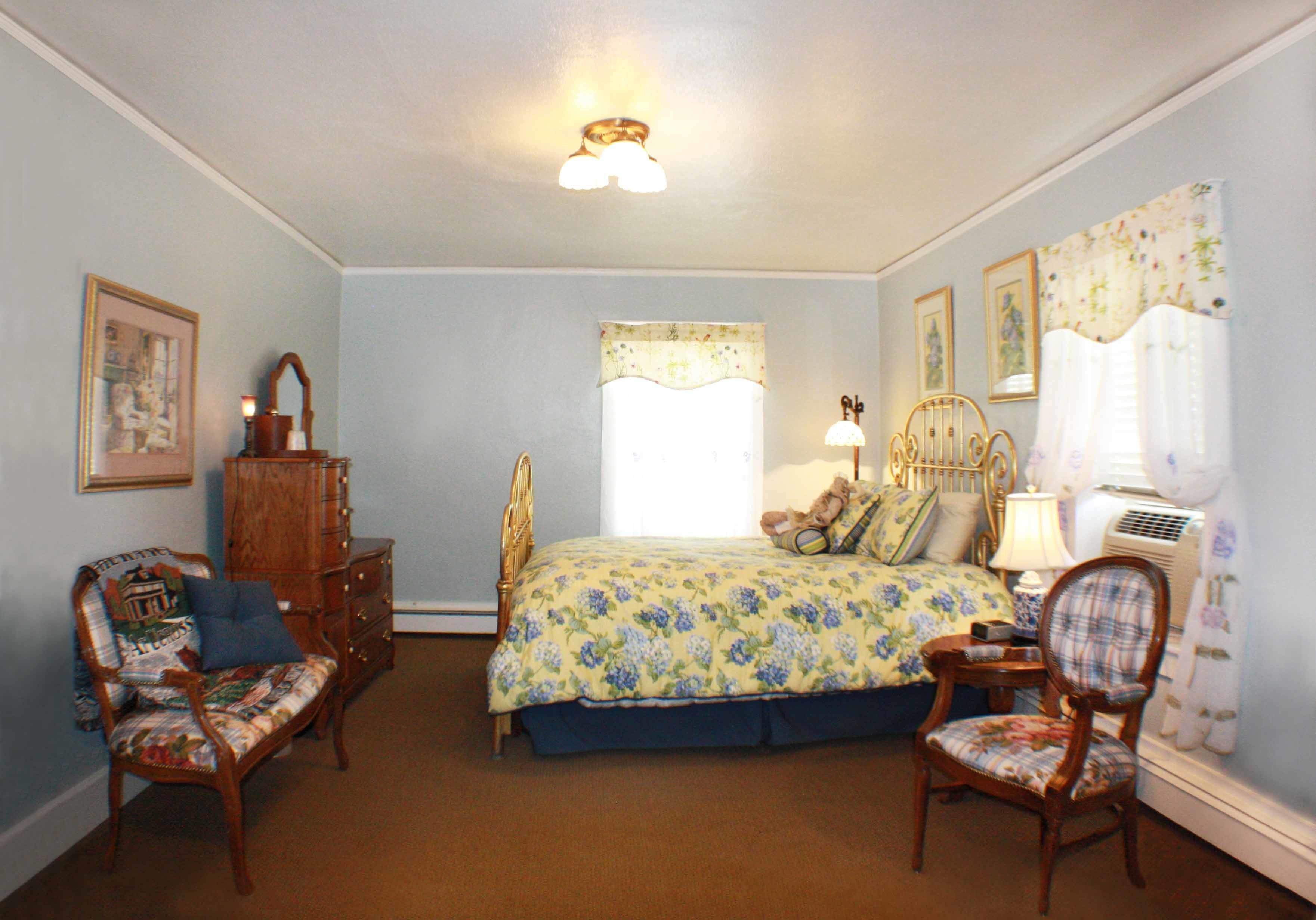 A bedroom with a bed, two chairs, a dresser, and a nightstand.