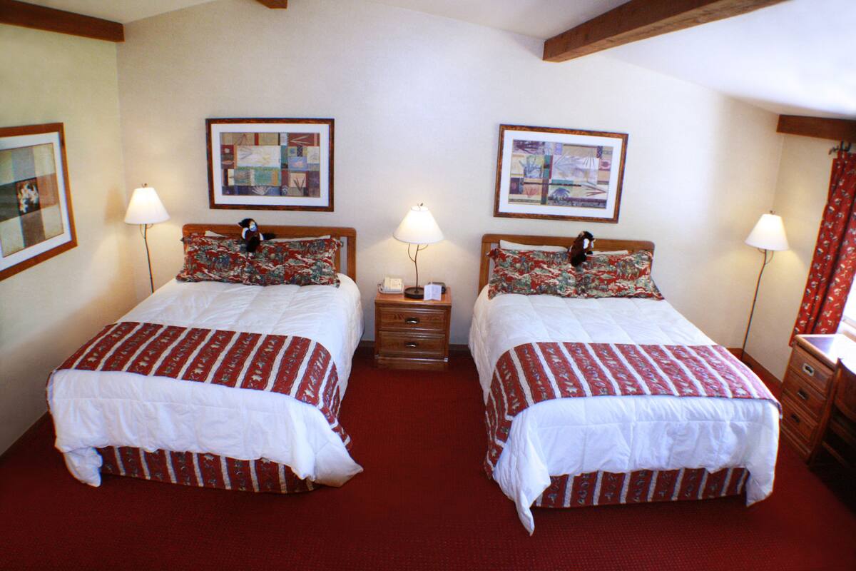 A double room with two beds, each with a floral-patterned bedspread and a white comforter. There are two bedside tables with lamps, and the room has a red carpet.