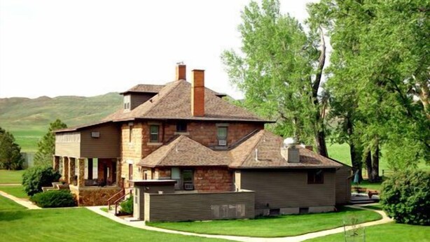 Una casa de dos pisos con fachada de piedra, un amplio porche delantero y un césped bien cuidado.