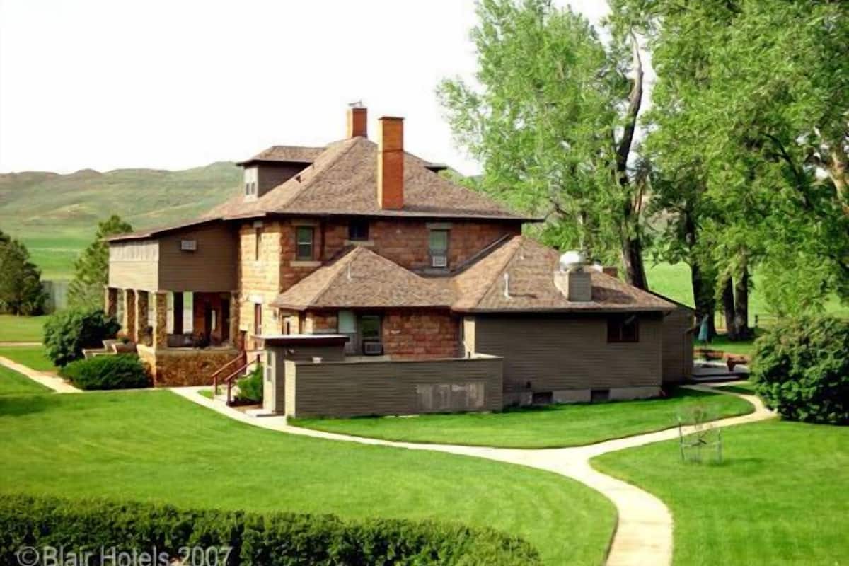 A two-story house with a stone facade, a large front porch, and a well-maintained lawn.
