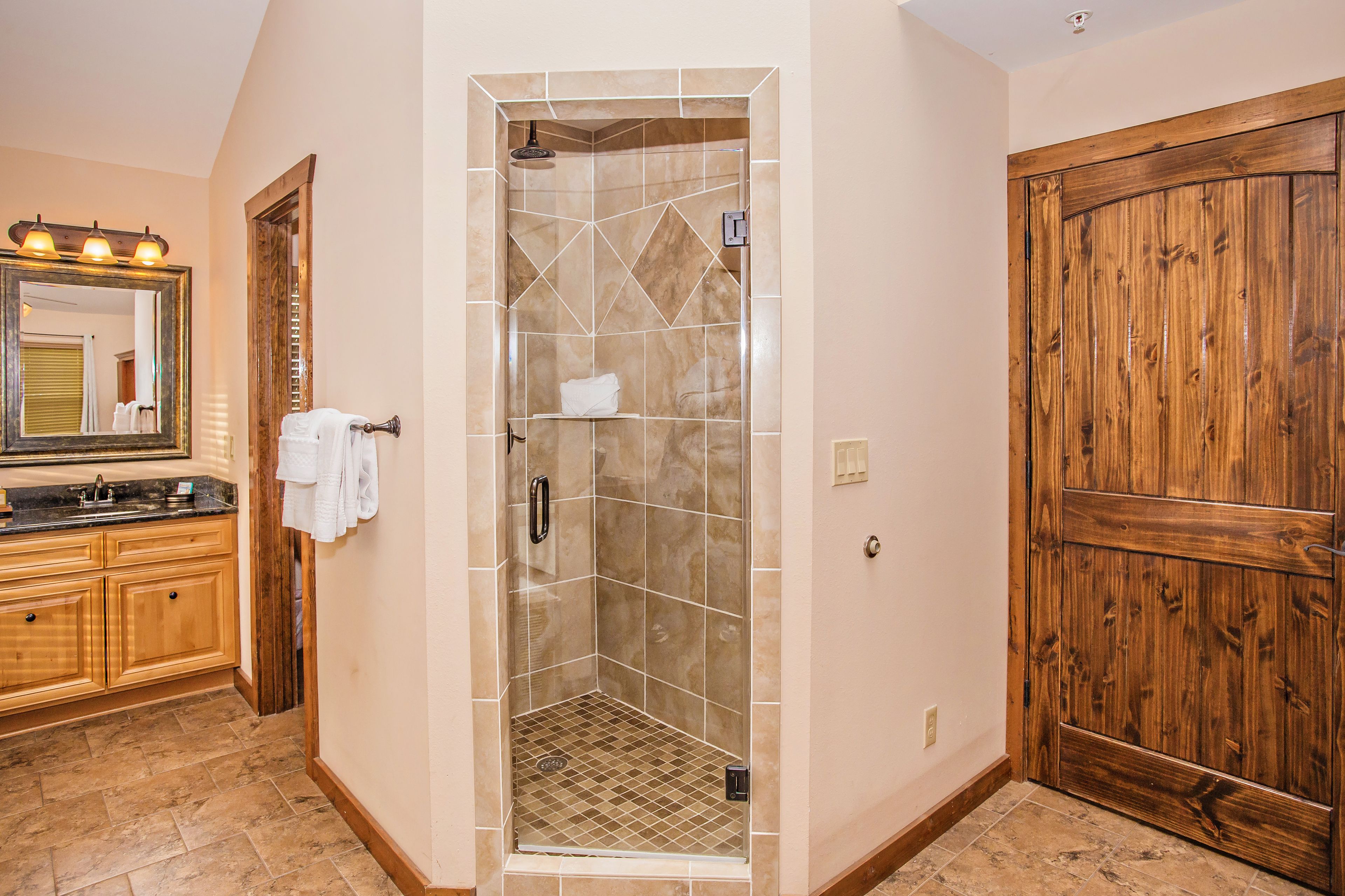 A bathroom with a glass-enclosed shower, wooden cabinets, a large mirror, and a wooden door.