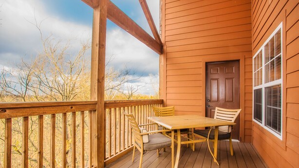 A wooden deck with a table and chairs, a door, and a window. - The Lodges at the Great Smoky Mountains (Pigeon Forge)