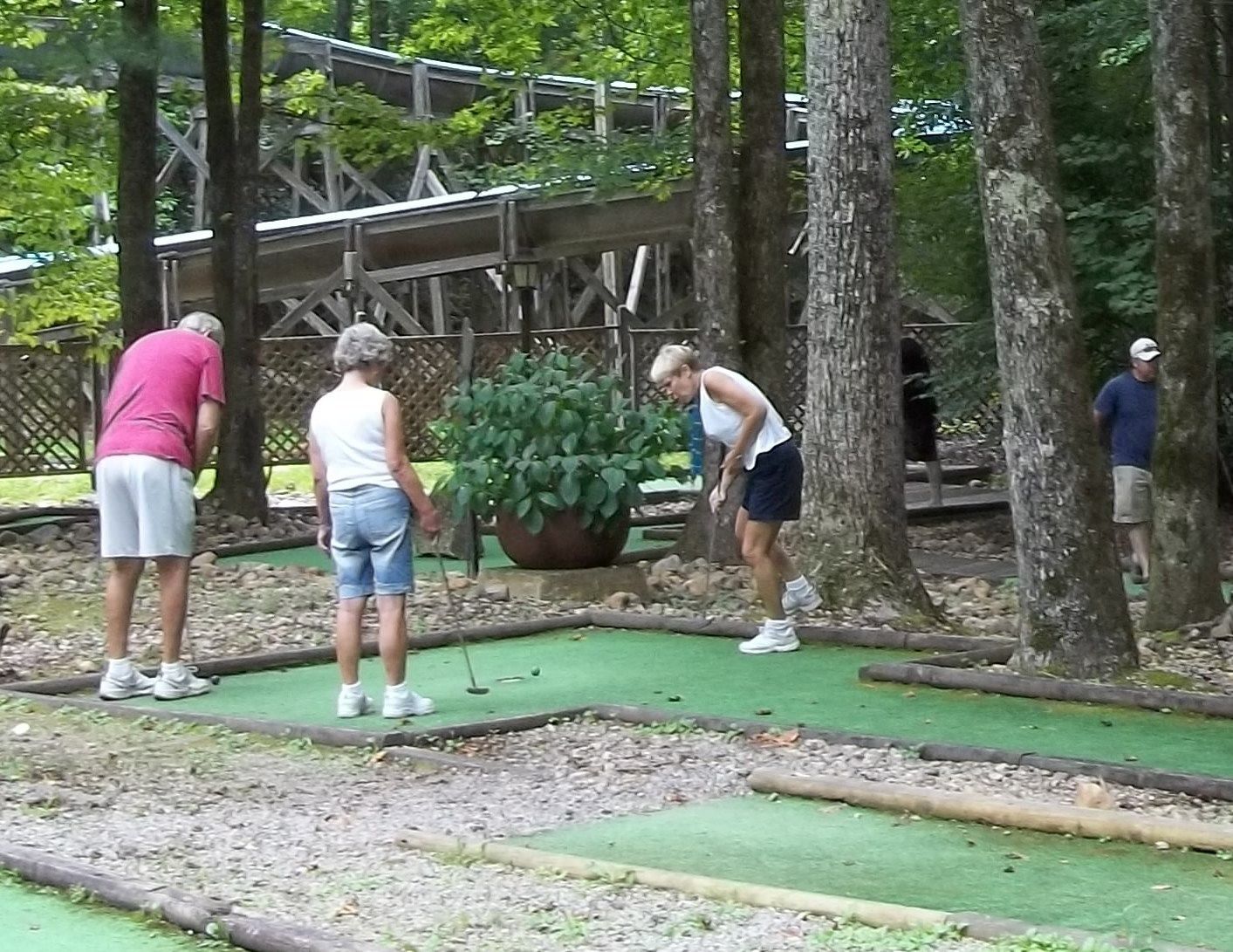 A group of people playing golf on a course with a wooden bridge in the background.