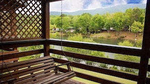 A wooden deck with a swing and a view of a river and greenery. - Country Hideaway at Mountain Lakes (Cleveland)