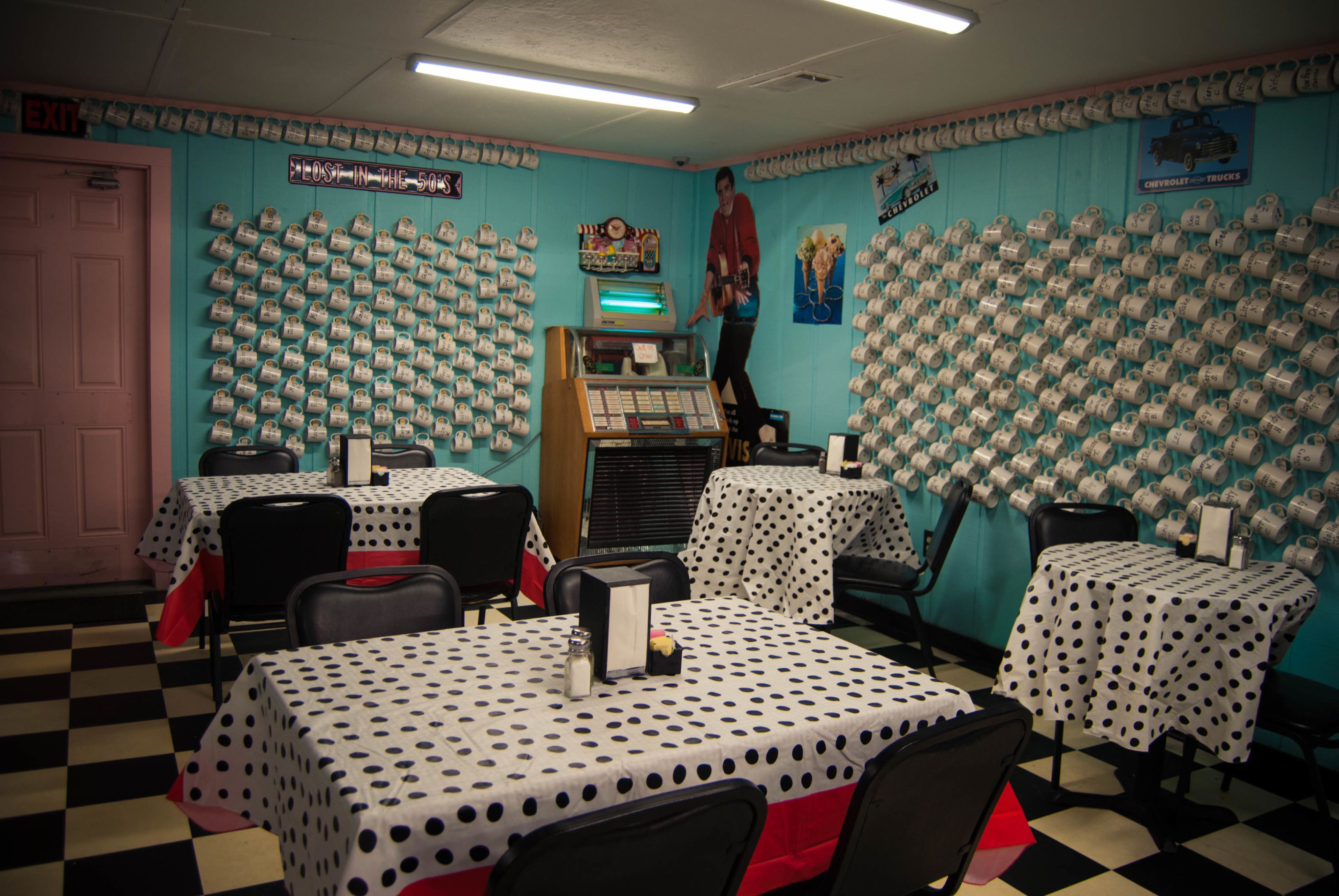 A restaurant with tables covered in polka dot tablecloths, a jukebox, and a wall decorated with vintage car mugs.